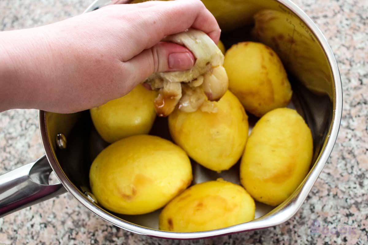 Hand squeezing the roasted garlic out of the casing and into the pan.