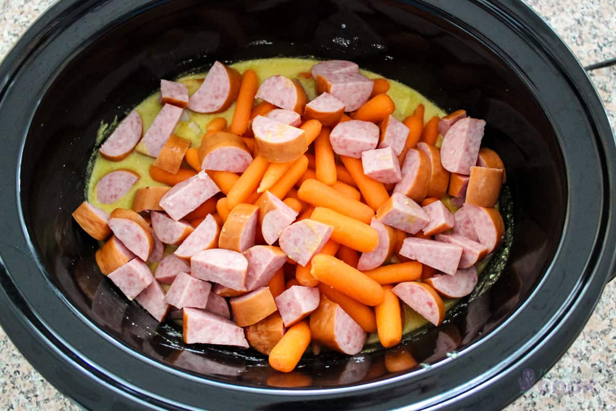 Sausage, onions, and carrots added to slow cooker insert.