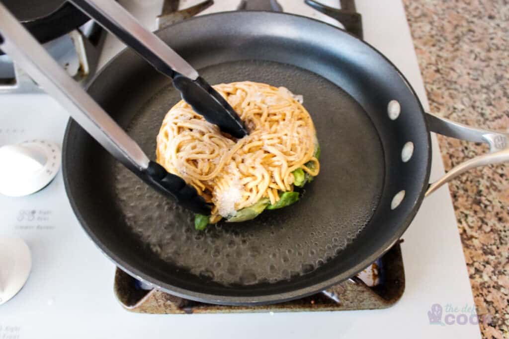 Noodle ring being added upside down to skillet of boiling water- noodles being held with tongs for safety.