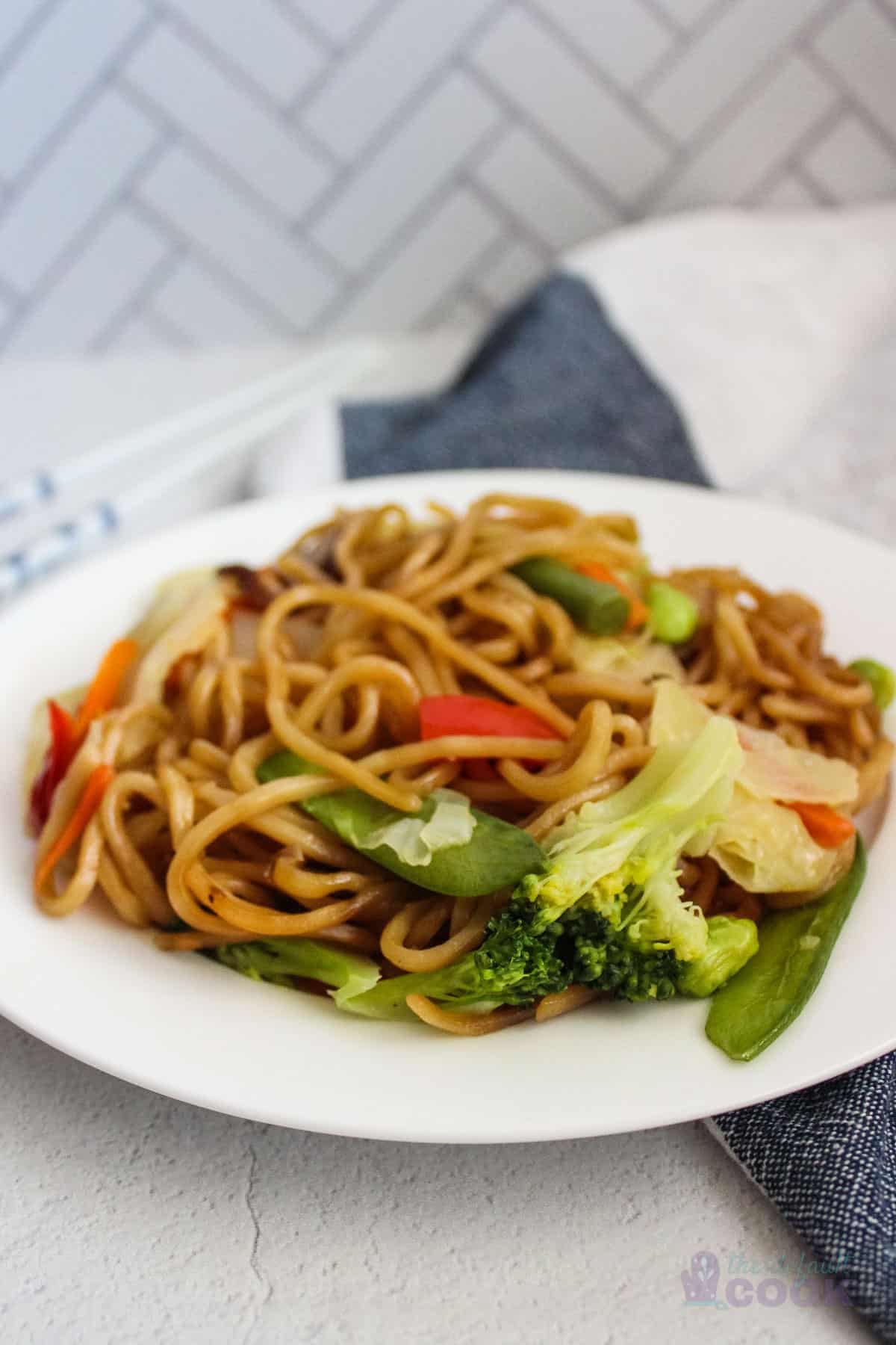 Plate of cooked costco yakisoba noodles on a blue and white kitchen towel on a counter.