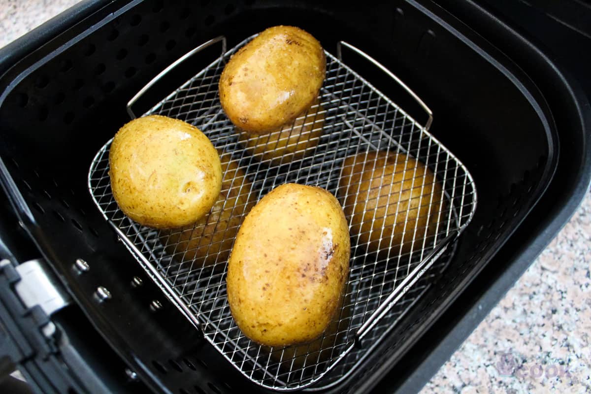 2 layers of prepared potatoes on a rack in a basket style air fryer.
