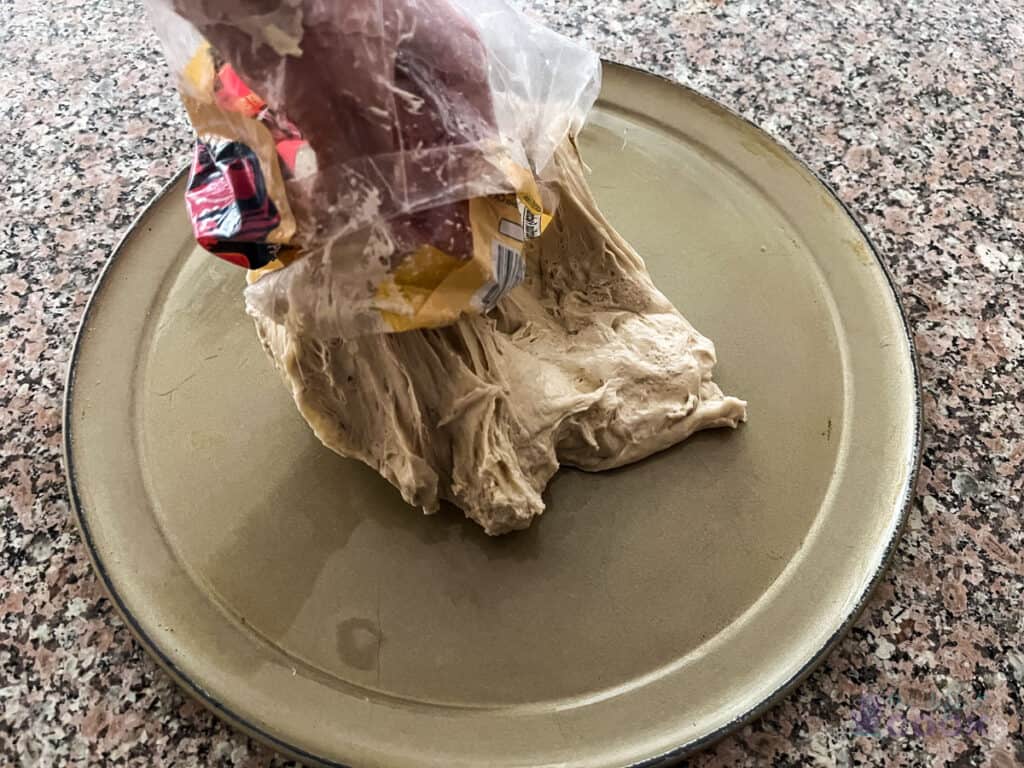 Pizza dough being transferred from the plastic bag it was bought in to the pan. Bag is inside out and hand pushing it to the pan using the bag as a barrier.