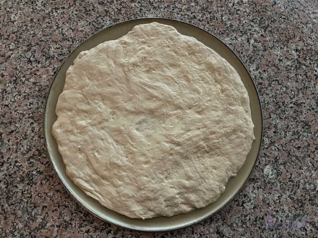 Raw pizza dough spread out on pizza pan.