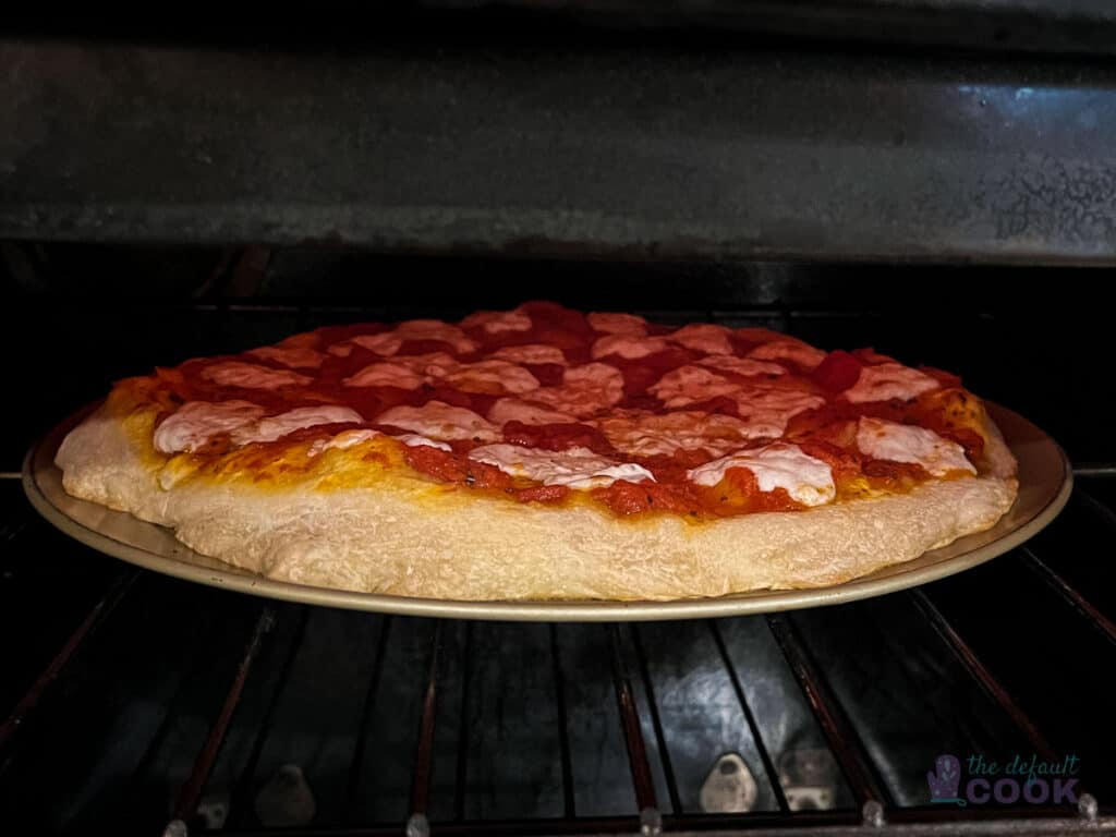 A pizza mostly cooked in the oven, with the broiler on to brown the cheese.