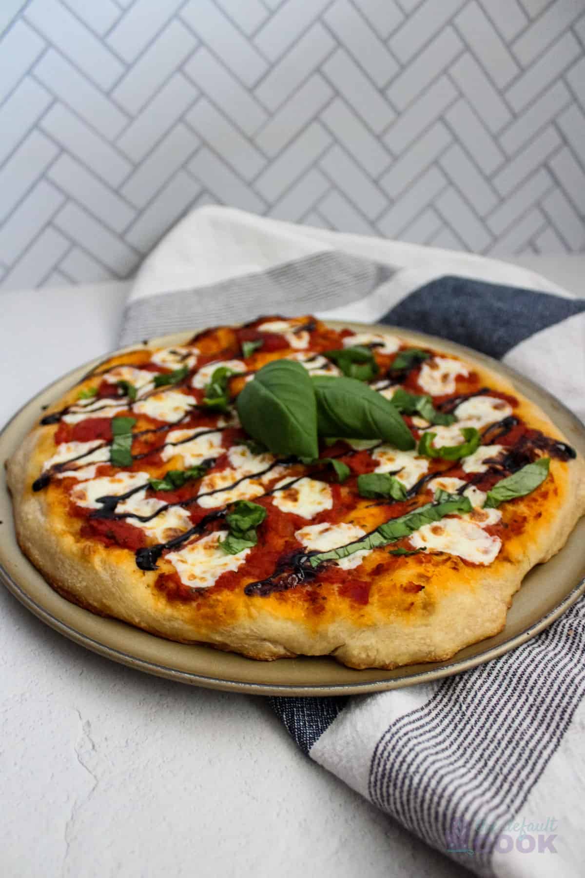 A whole bruschetta pizza on the baking pan with a tea towel.