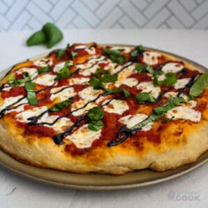 Pizza on the pan with basil behind it, both on a white marble surface with chevron tile backsplash in the background.