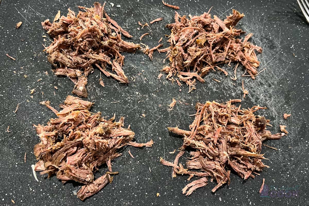 Four small piles of shredded pot roast on a cutting board.