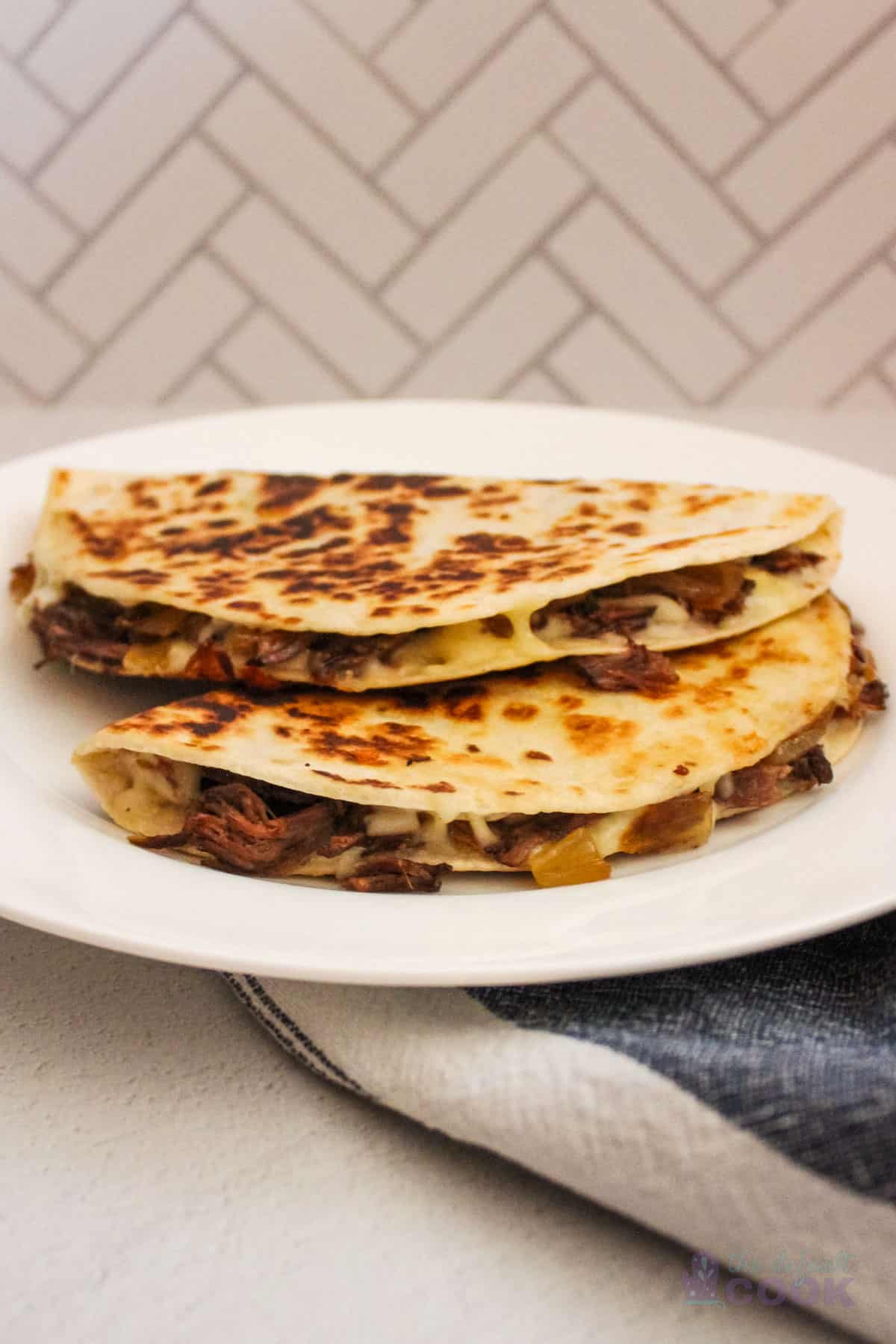Two leftover pot roast quesadillas stacked on a white plate.