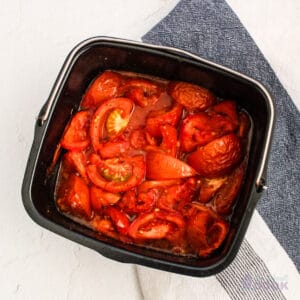 A black pan with roasted tomatoes in it on a white and blue surface.