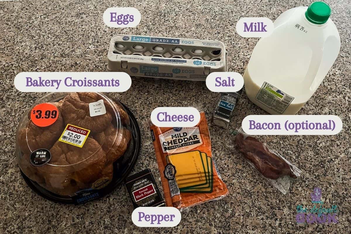 Labeled ingredients on a kitchen counter: croissants, cheese slices, eggs, milk, cooked bacon, salt, and pepper.