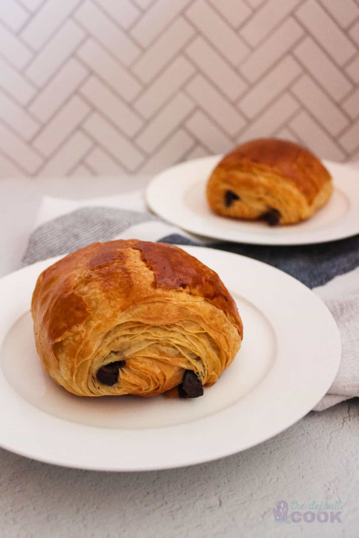 Two plates with a croissant each on them on a counter with a kitchen towel.