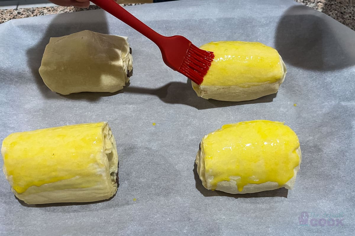 4 risen croissants on a parchment lined baking sheet with the third being egg washed.