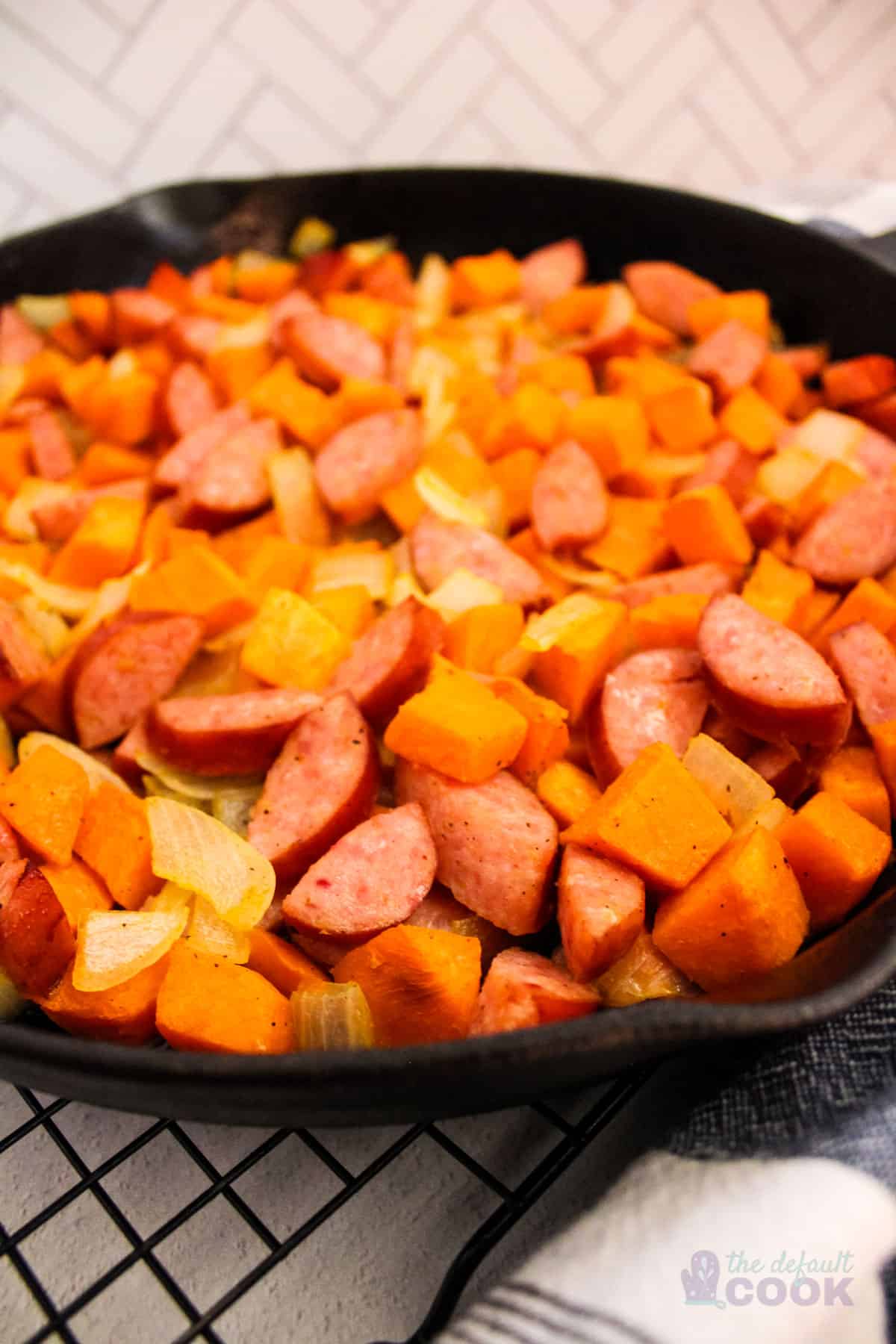 Close up of an iron skillet filled with cooked sweet potatoes, smoked sausage, and onions.