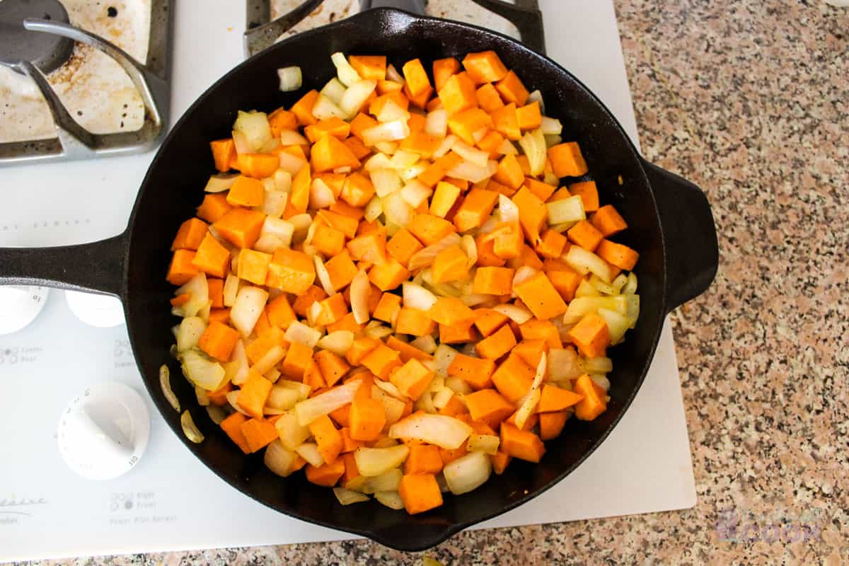 Sweet potatoes and onion cooking in a skillet on the stove.