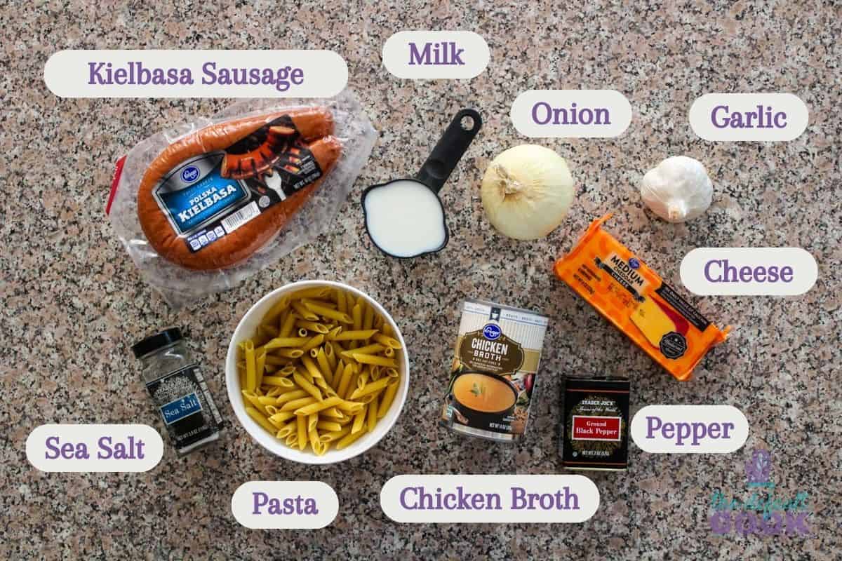 Ingredients on a kitchen counter labeled: sausage, milk, onion, garlic, cheese, pepper, broth, pasta, and salt.