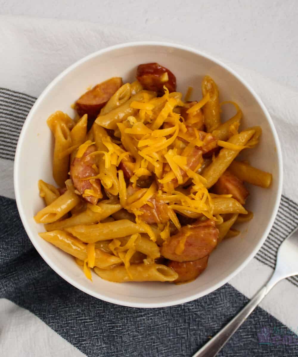 Cheesy pasta with smoked sausage and onions in a white bowl.