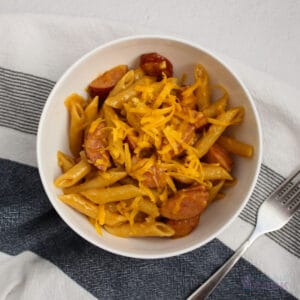 Cheesy pasta with smoked sausage and onions in a white bowl.