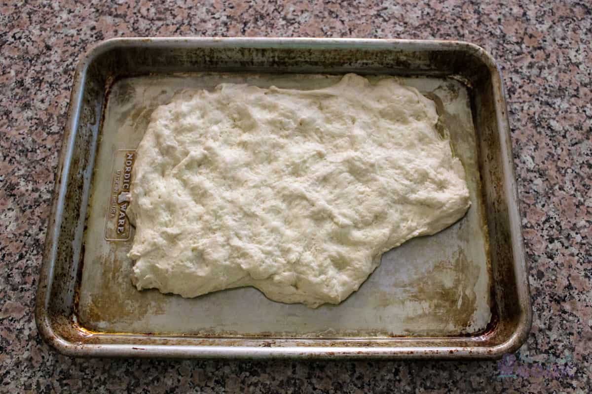 Pizza dough on a greased quarter sheet pan.
