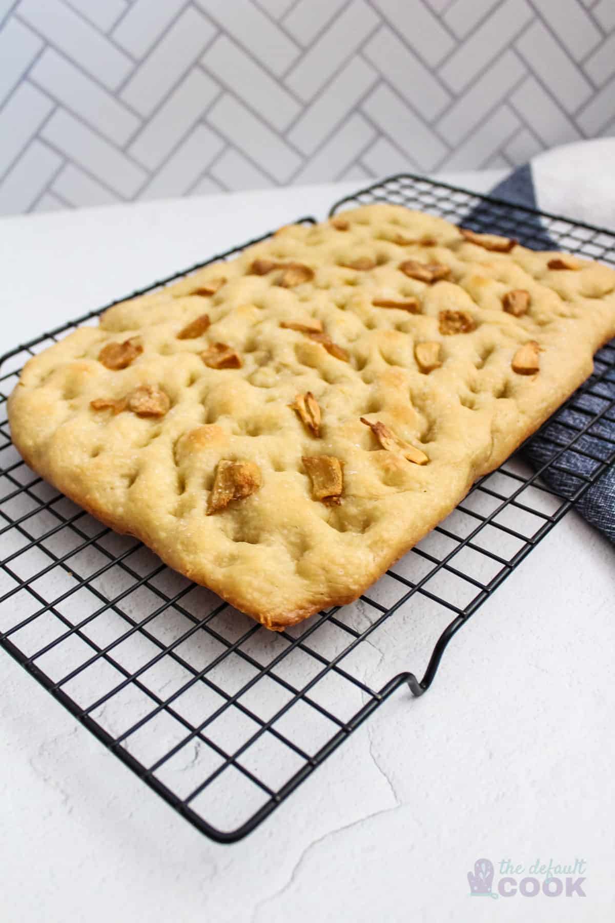 Focaccia bread with roasted garlic sitting on a cooling rack on a counter.