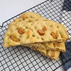 Sliced focaccia bread with roasted garlic topping on a cooling rack.