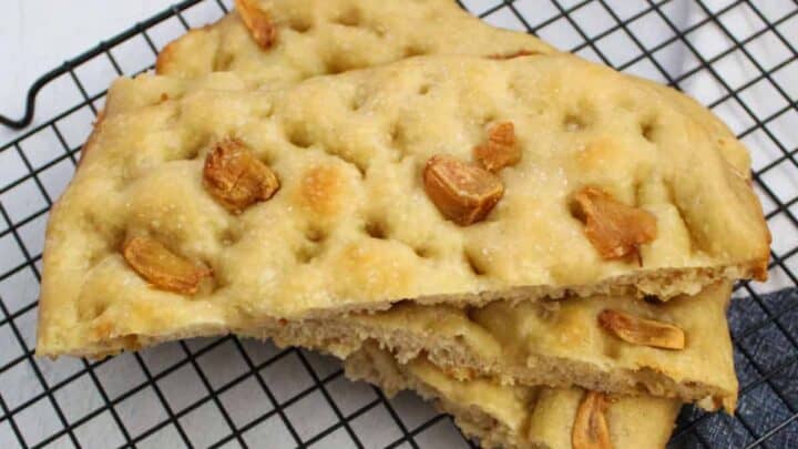 Sliced focaccia bread with roasted garlic topping on a cooling rack.