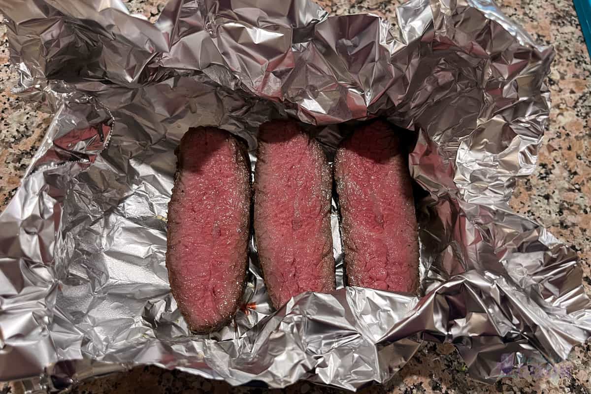 Three slices of tri tip in a pocket of aluminum foil.