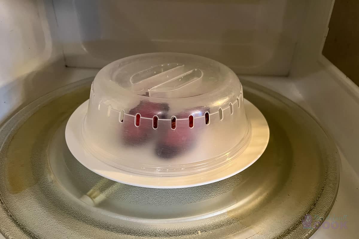 Two slices of tri tip on a white plate with a microwave cover over it, sitting inside a microwave.