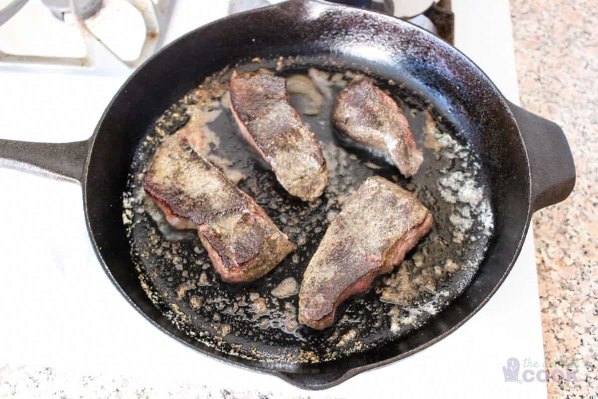 4 short ribs in a cast iron skillet browning.
