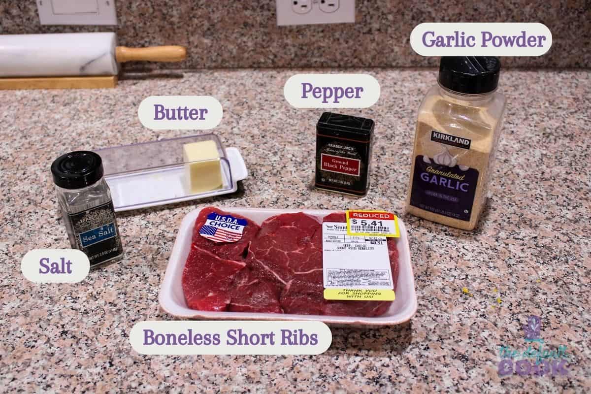 Labeled ingredients on a kitchen counter: boneless beef short ribs, salt, pepper, garlic powder, and butter.