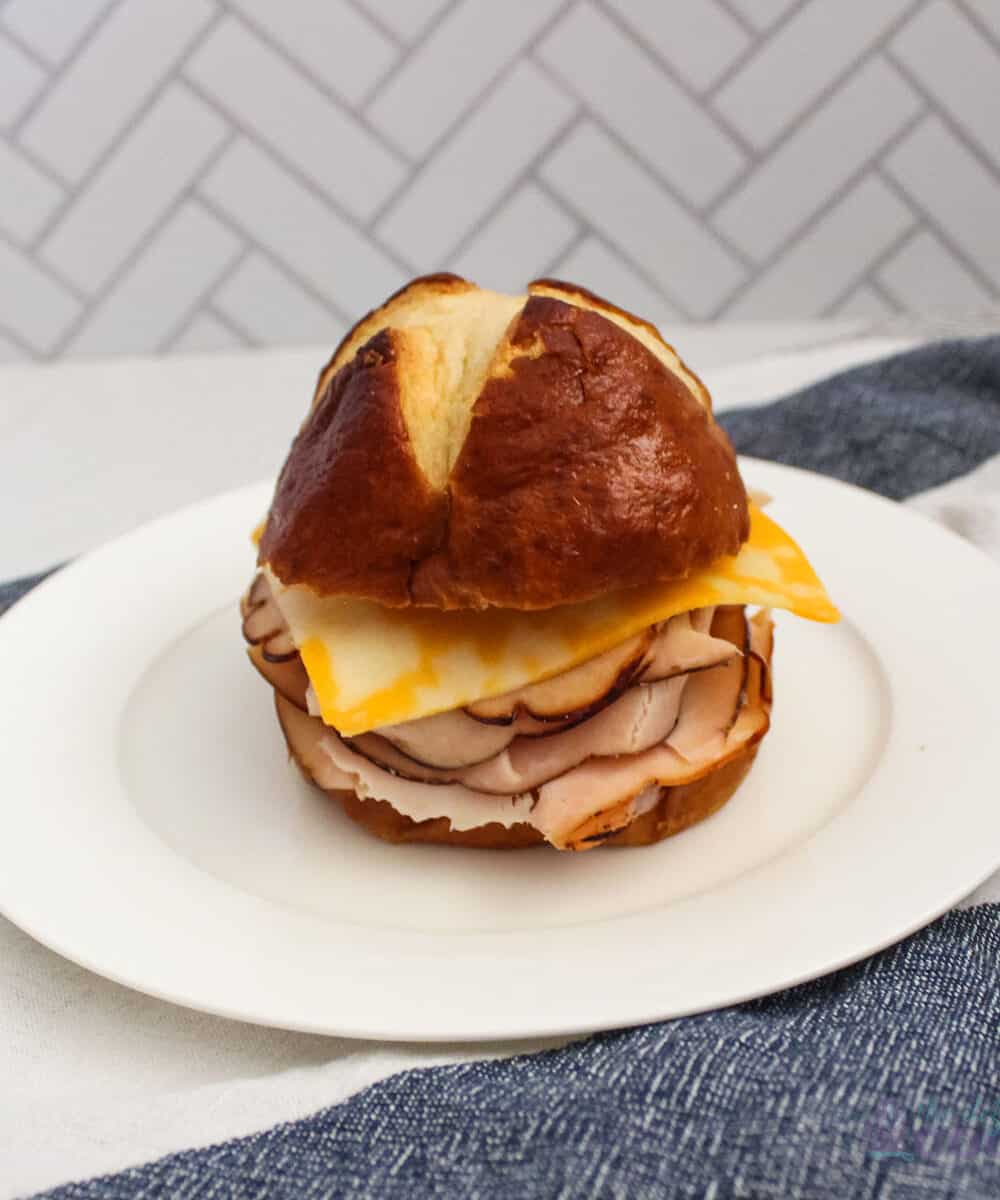 Pretzel bun sandwich with turkey and cheese on a white plate.