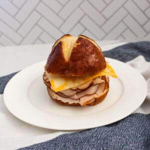 Pretzel bun sandwich with turkey and cheese on a white plate.