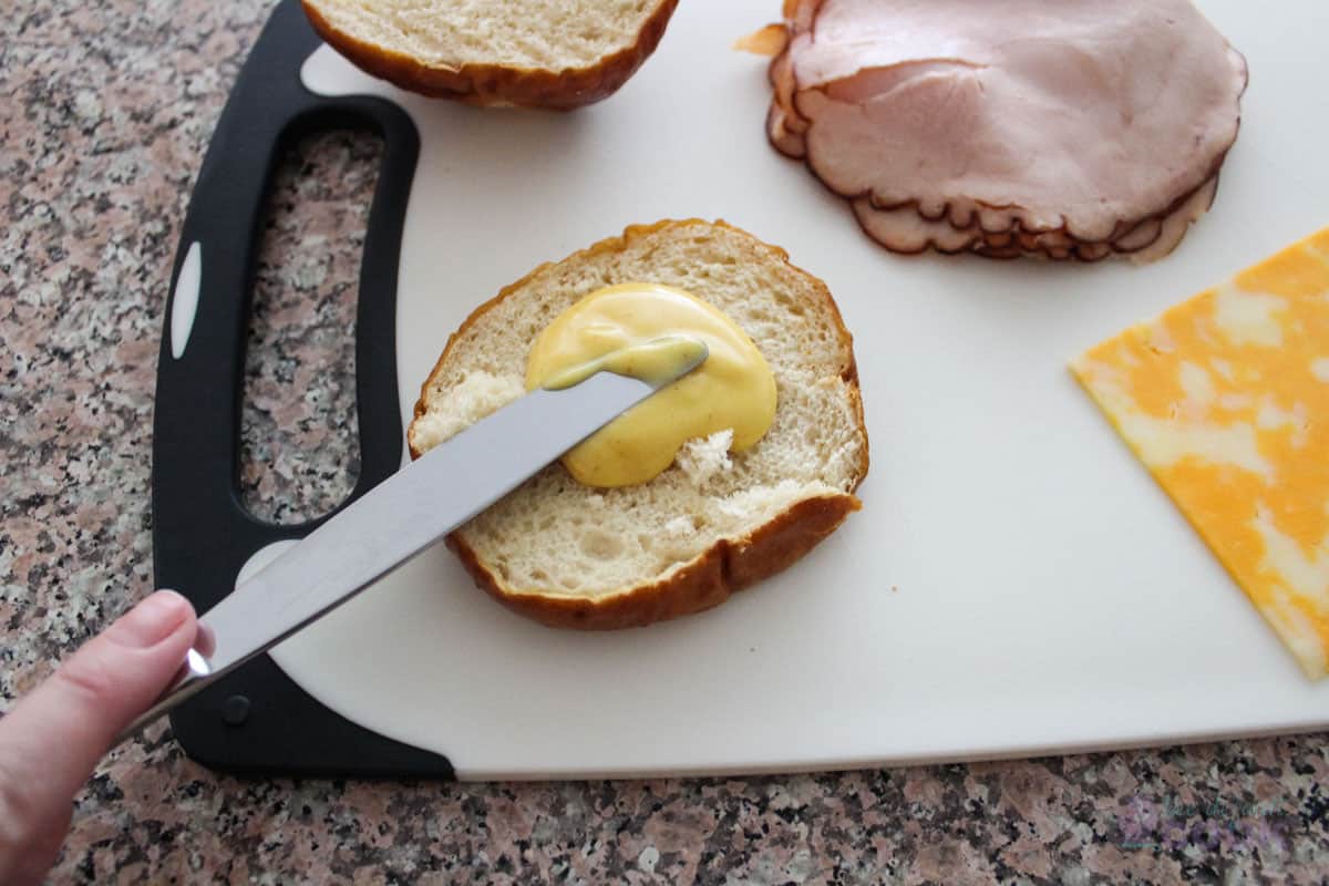 Spreading honey mustard on the bottom half of the pretzel bun.