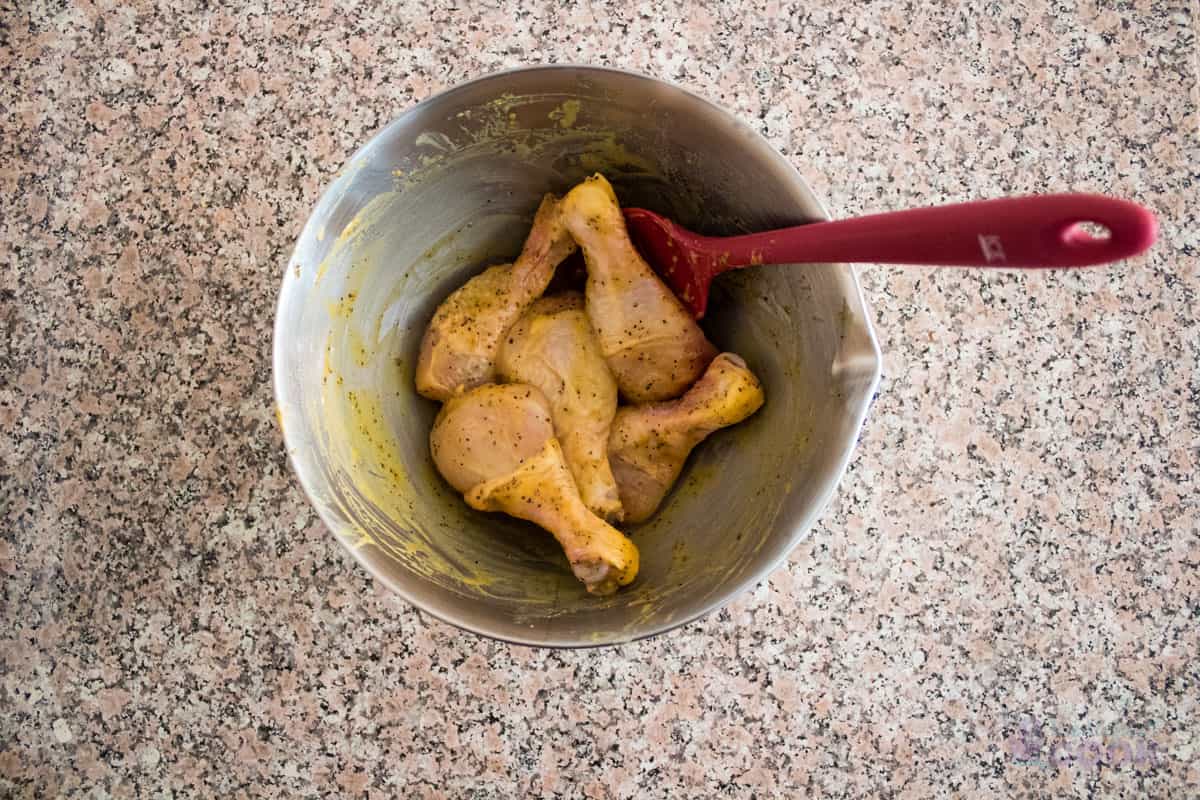 Bowl with chicken legs and seasonings mixed with a spatula that is still in the bowl.