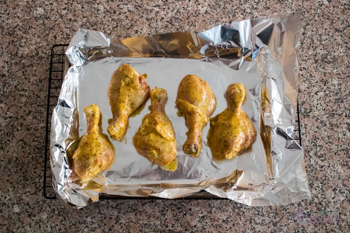 Uncooked, prepared drumsticks on a quarter sheet baking pan lined with aluminum foil.