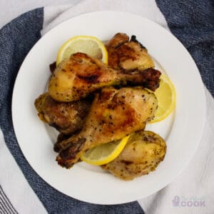 Overhead shot of 5 chicken legs with lemon slices between them on a white plate.