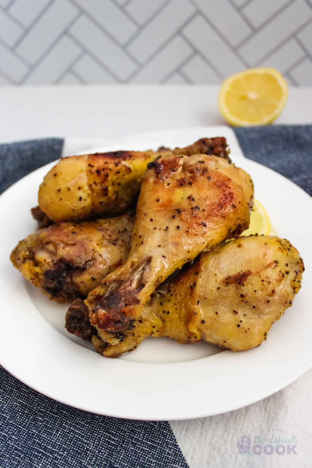 A plate of chicken legs with lemon slices in the back on a white and blue kitchen towel.