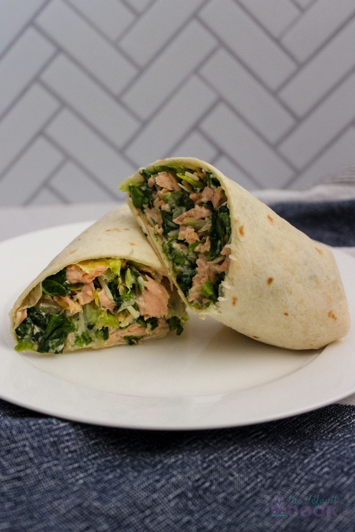 Salmon wrap sliced in half with one half leaning on the other on a white plate on top of a blue and white kitchen towel.