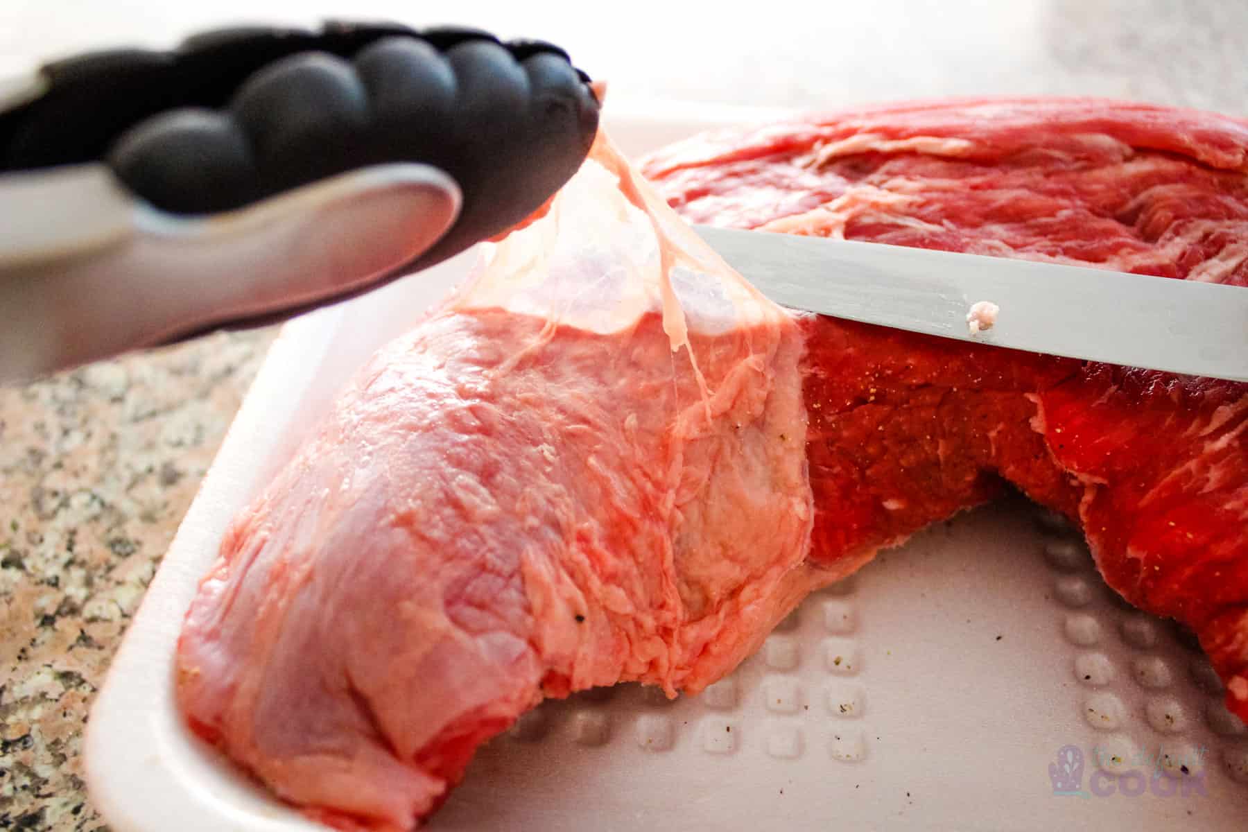 Silver skin being separated from a tri tip with a knife and tongs.