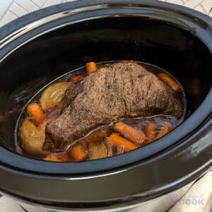 Finished tri tip roast in a slow cooker on a bed of carrots and onions.