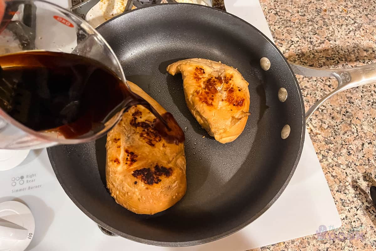 Chicken searing in a pan with the first seared side up, and sauce being poured into the pan with the chicken.