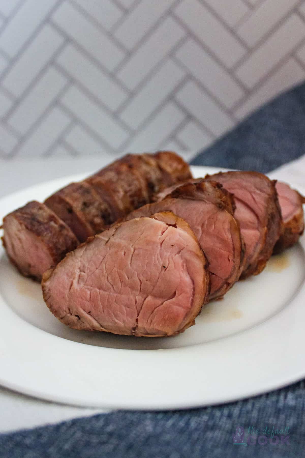 A pork tenderloin sliced and presented on a white plate with a kitchen towel below it.