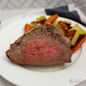 Sliced tri tip on a white plate with potatoes and carrots.