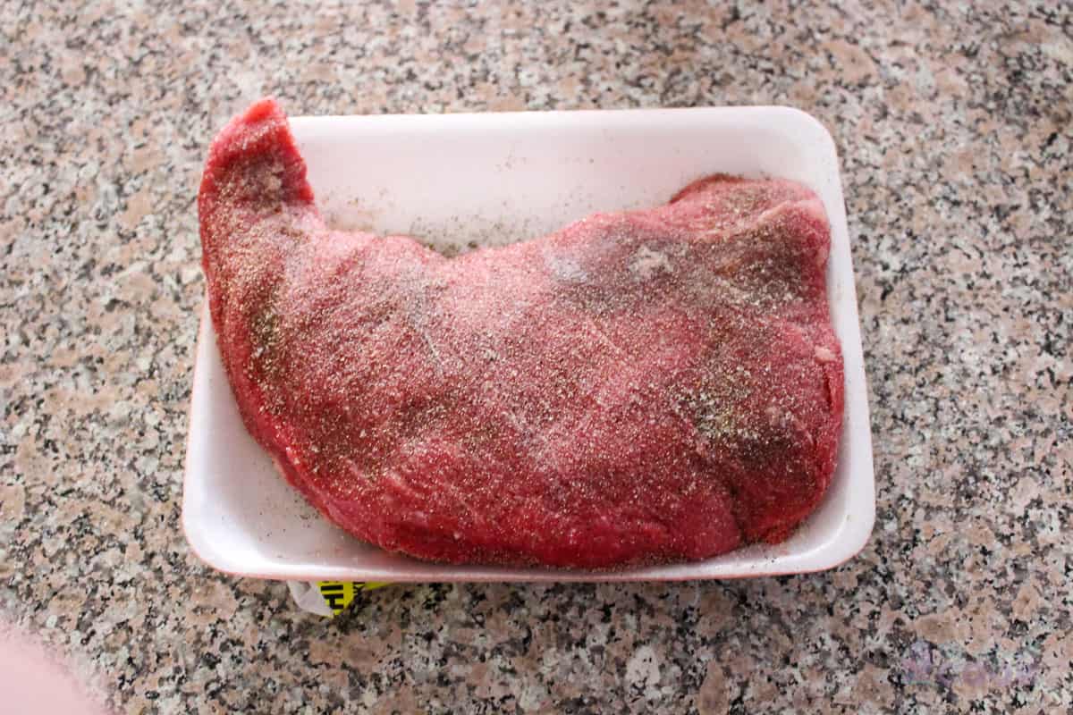 Raw tri tip roast seasoned with salt, pepper, and garlic powder.