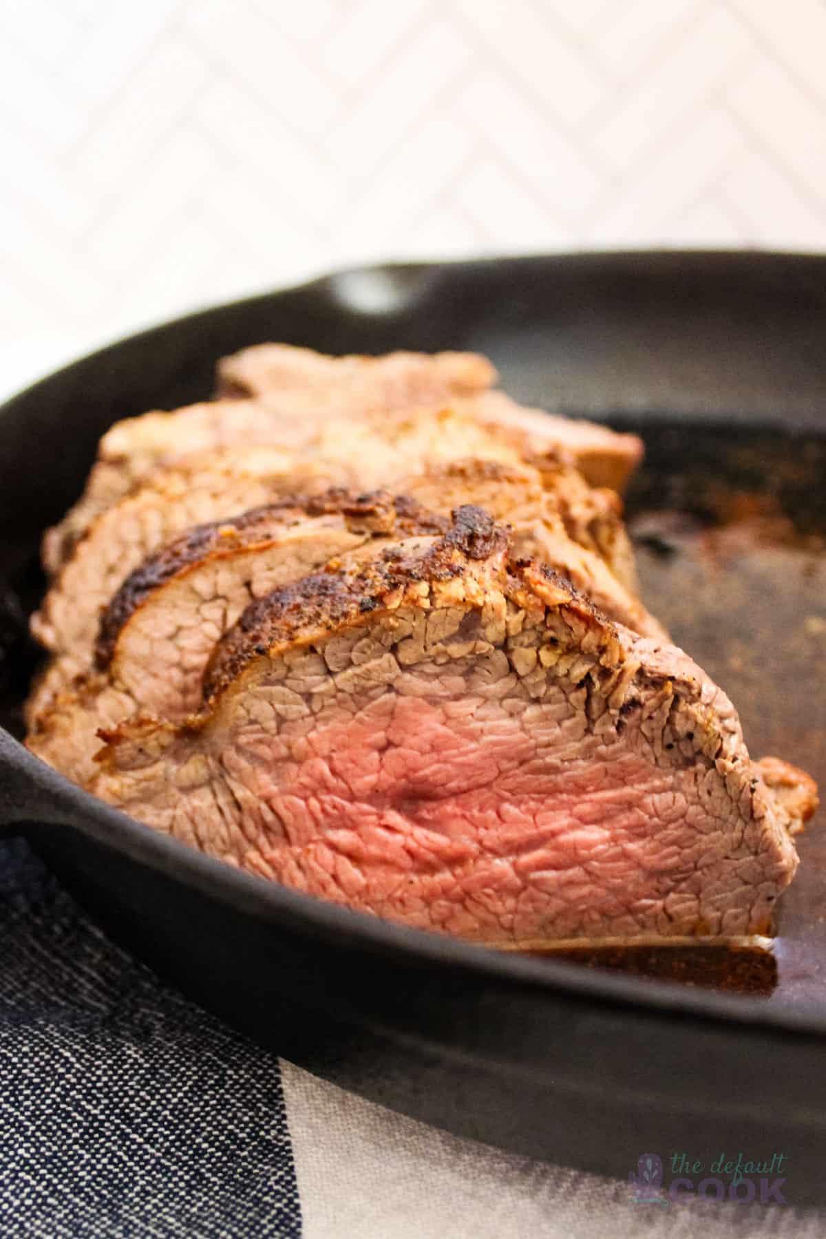 Sliced tri tip in a cast iron skillet on a blue and white kitchen towel.