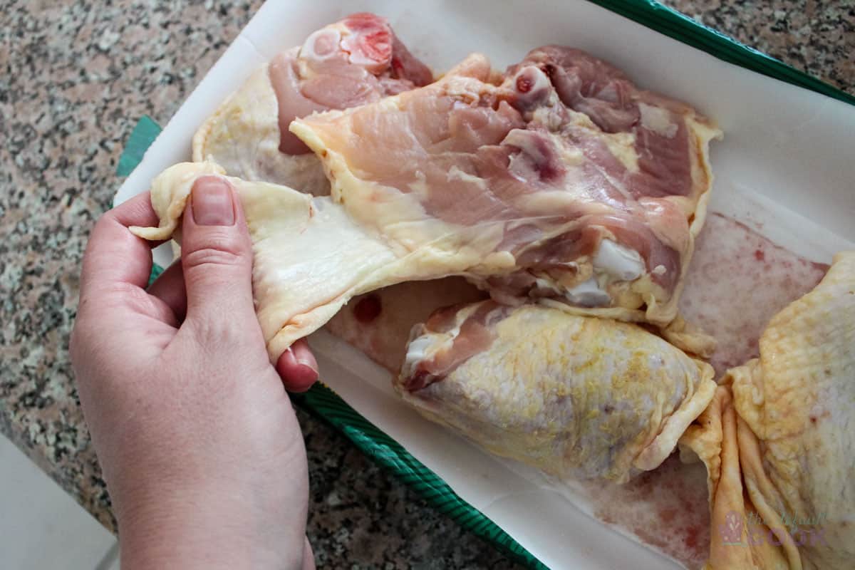 A hand holding the skin that was covering the bottom of a chicken thigh for trimming.