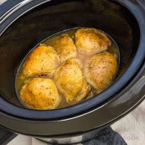 6 cooked lemon pepper chicken thighs in a black oval slow cooker.