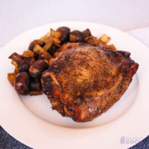 A chicken thigh, onions, and mushrooms on a white plate.