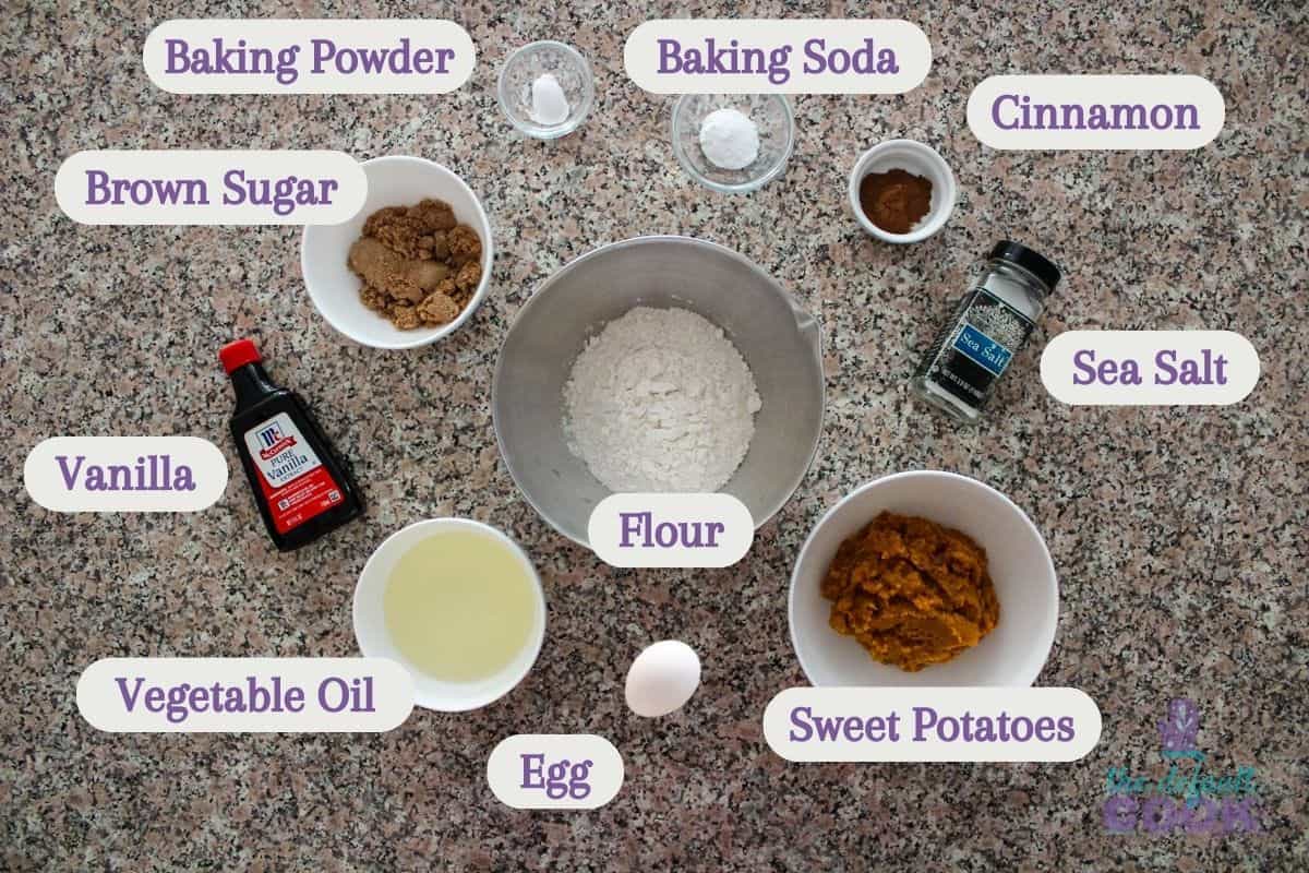 Labeled ingredients on a kitchen counter: vanilla, brown sugar, baking powder, baking soda, cinnamon, salt, flour, vegetable oil, egg, and mashed sweet potatoes.