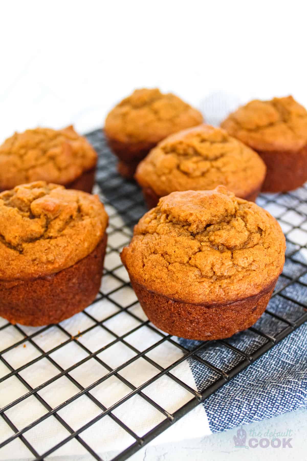 Six sweet potato muffins on a wire rack on top of a kitchen towel.