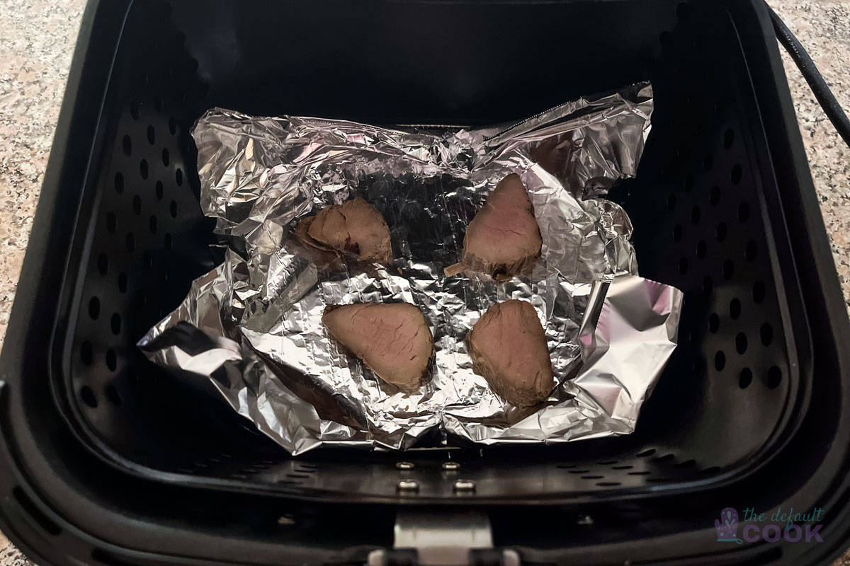 Four slices of pork tenderloin in aluminum foil sitting in an air fryer basket.